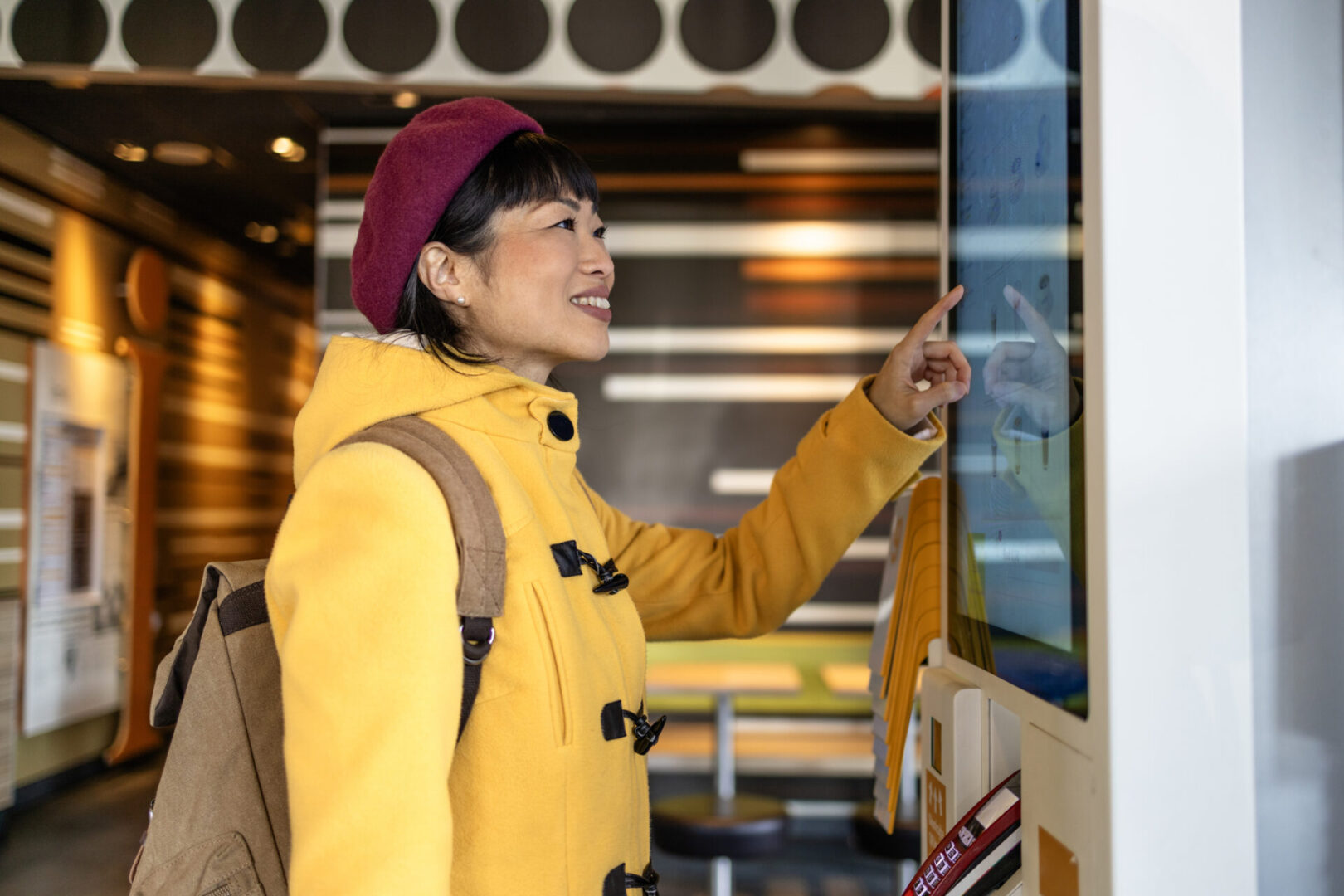Smiling woman in yellow coat at touchscreen